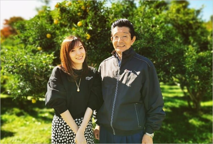 ゆずの果樹を背景に、高橋麻里江さんと松本広行さんがにこやかに並んでいる写真